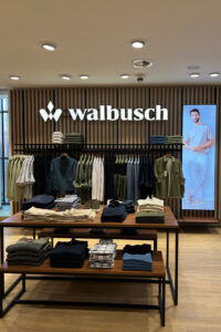 Die Markenwand mit beleuchtetem Walbusch-Logo und digitalem Screen bildet den visuellen Anker der Fläche
